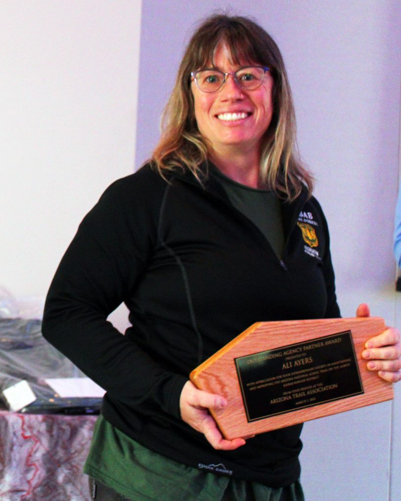A woman in a black fleece with glasses and brown hair holding an award