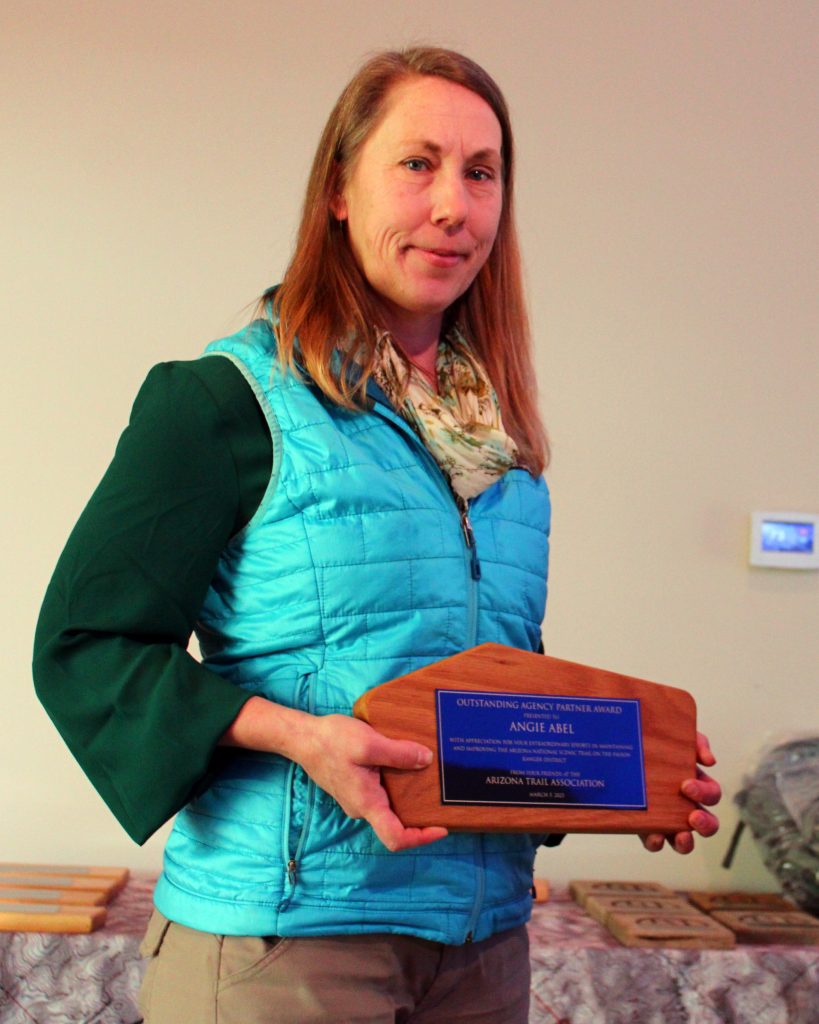 A woman in a blue puffy vest and a small smile holding an award