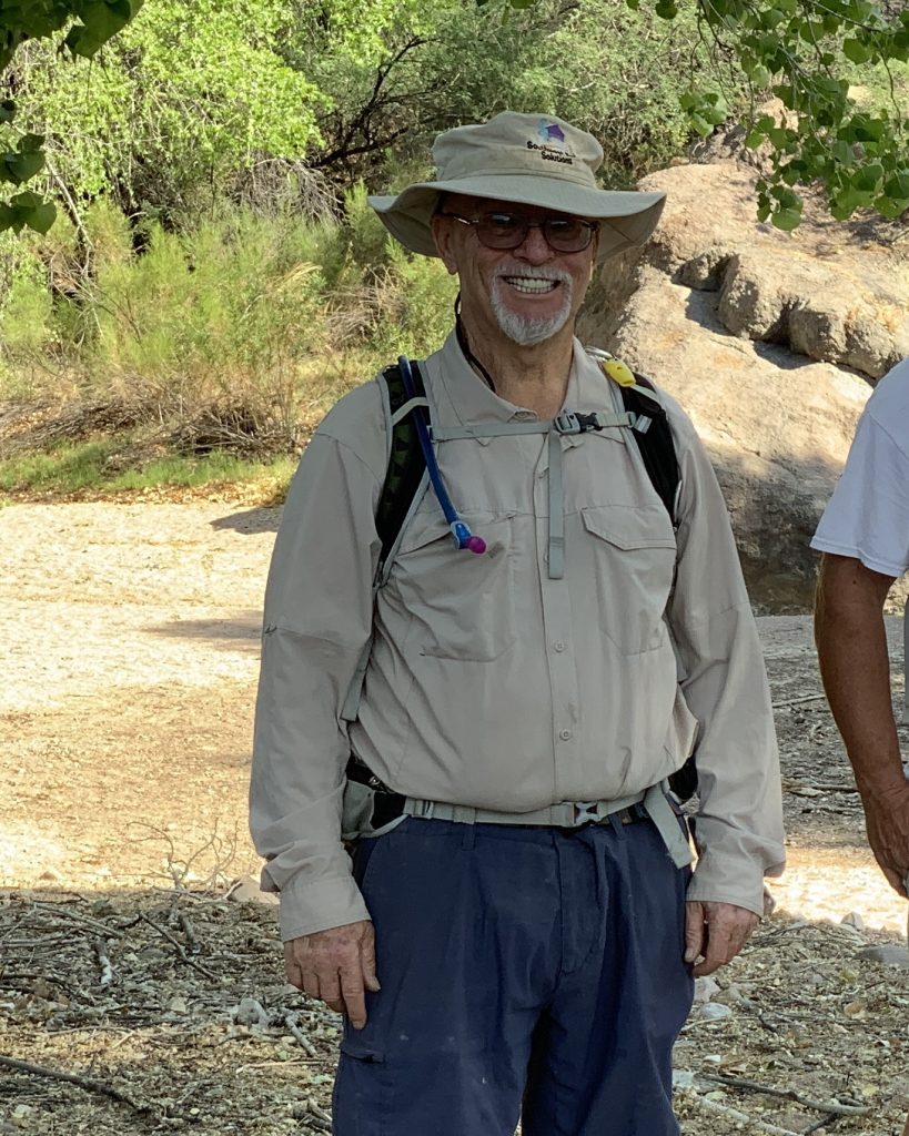 A man with a grey beard and a bucket hat standing in the desert