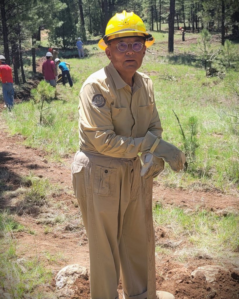 A man in a yellow hard hat holding a tool in the forest 