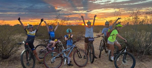 Girls celebrating on mountain bikes with the sunset behind them